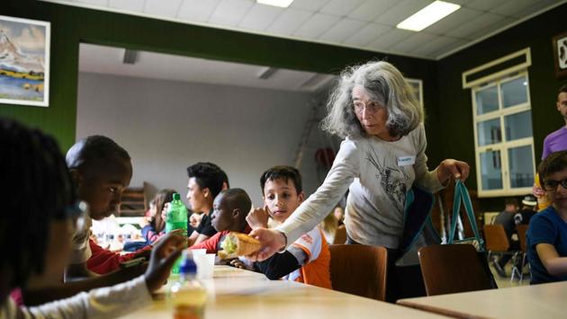 A volunteer (R) distributes sandwiches to refugee children at the temporary accommodation. Elisabeth Schulthess, head of Neighbours Around the World said that they try to involve the migrants into the local life of the town. But Schulthess complains there is very little in the way of social support. In 2018, 54 % of the 141 people who came won the status of refugee or subsidiary protection in France. (Sebastien Bozon / AFP) 