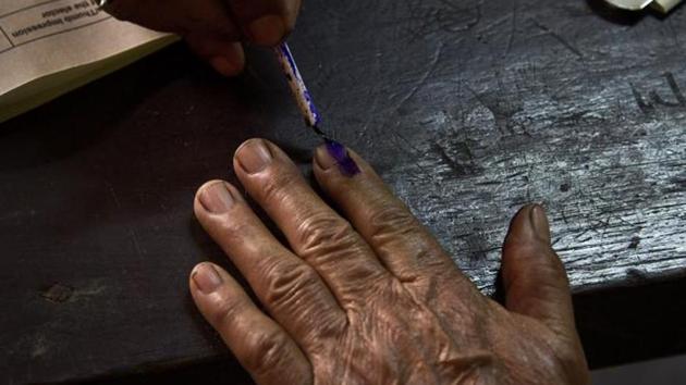 An election officer puts indelible ink mark on the index finger of an elderly voter at a polling centre.(AP)