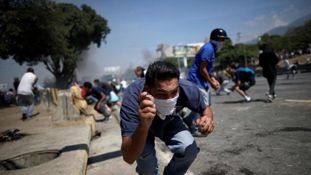 An opposition demonstrator crouches down, holding rocks, on a street near the Generalisimo Francisco de Miranda Airbase “La Carlota” in Caracas, Venezuela. (Ueslei Marcelino / REUTERS)