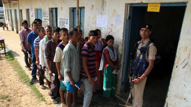 Tripura, April 23 (ANI): A CRPF officer stands guard at the polling station as the voters in a queue to cast vote during the general election at village Hajaripara in Agartala on Tuesday. (ANI Photo)