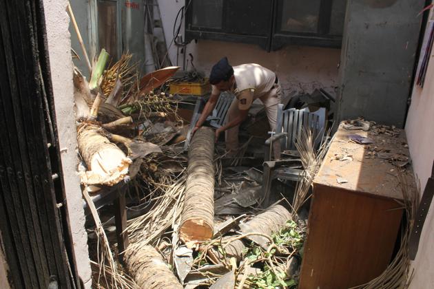 A policeman removes the trunk and branches of the coconut tree that fell on the roof of the Thane rural police drivers’ restroom at Court Naka.(Praful Gangurde/ HT Photo)