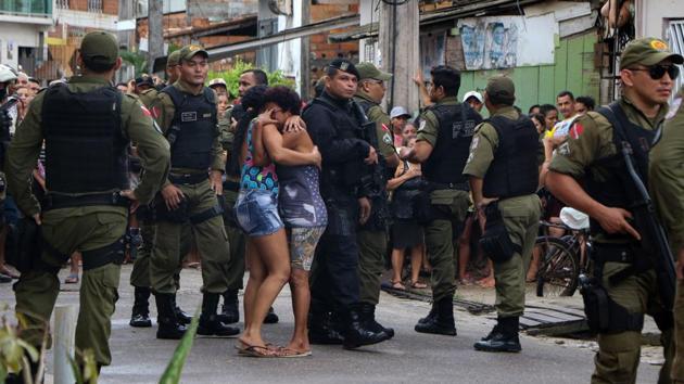 Residents mourn surrounded by police officers outside a bar as corpses are removed after a shooting, in Belem, Para state, Brazil. At least 11 people were shot dead when unknown men opened fire. (Claudio Pinheiro / Agencia Panamazonica / AFP)