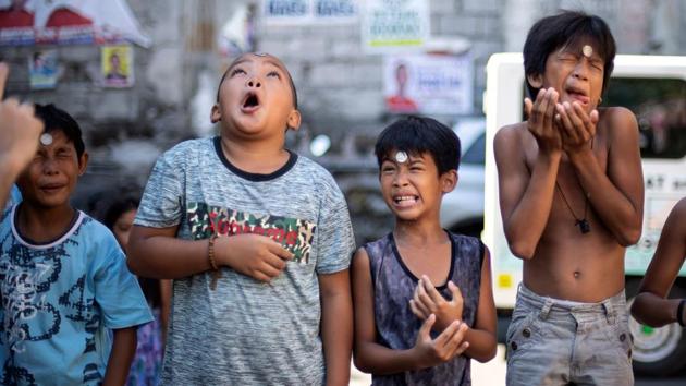 Boys contort their faces as they participate in a game where they need to slide a coin from their forehead to their mouth to win, during the annual Feast Day of St. Rita of Cascia in Manila, Philippines. (Noel Celis / AFP)