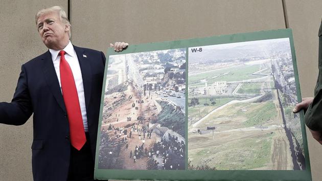 US president Donald Trump holds a poster with photographs of the US. - Mexico border area as he reviews border wall prototypes in San Diego with Rodney Scott.(AP Photo)