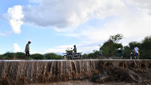 People wade across a submerged road following flash flooding in Isiolo. With conditions ever-more unreliable, technology has replaced warriors once dispatched to scout for grazing land. “They wake up very early in the morning and they look at the clouds, they look at the moon, to predict. I use this now,” Hassan said, scrolling through customised weather updates on her phone, sent via SMS. (Tony Karumba / AFP) People wade across a submerged road following flash flooding in Isiolo. With conditions ever-more unreliable, technology has replaced warriors once dispatched to scout for grazing land. “They wake up very early in the morning and they look at the clouds, they look at the moon, to predict. I use this now,” Hassan said, scrolling through customised weather updates on her phone, sent via SMS. (Tony Karumba / AFP)