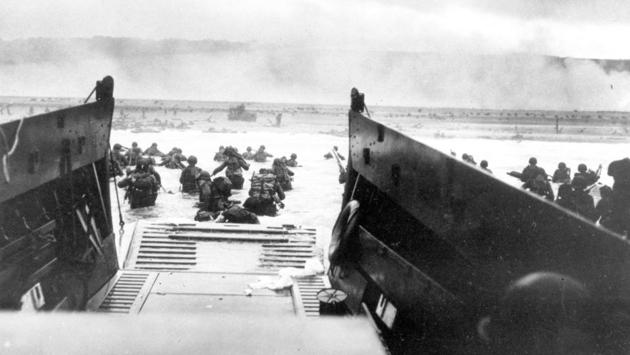 Under heavy German machine gun fire, American infantrymen wade ashore off the ramp of a Coast Guard landing craft during the invasion of the French coast of Normandy in World War II. June 6, 2019, marks the 75th anniversary of D-Day, the assault that began the liberation of France and Europe from German occupation, leading to the end World War II. (US Coast Guard via AP)