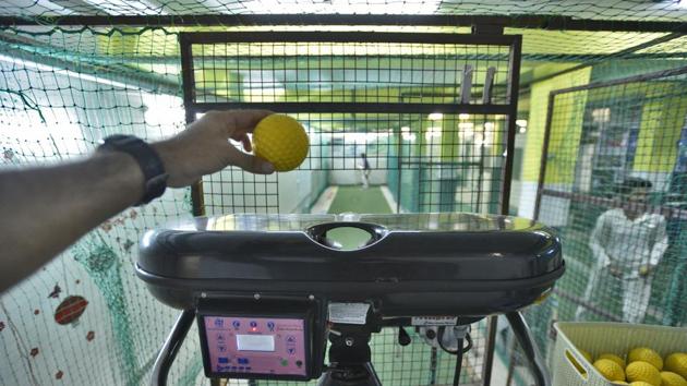 A bowling operator loads a ball on to the bowling machine inside an indoor cricket facility. In a country like India overwhelmed with cricket and icons like Sachin Tendulkar and Yuvraj Singh to name a few, most of young cricketers aspire to become batsman making these cricket academies with automated bowling facility very popular. (Burhaan Kinu / HT Photo) 