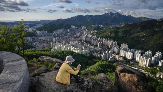 A woman looks at her phone, sitting on top of rocks from where the Seoul skyline can be seen in the background in South Korea. (Ed Jones / AFP)