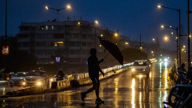 A man crosses a road with an umbrella as it rains at Marine Drive in Mumbai, Maharashtra. (Ragul Krishnan / HT Photo)