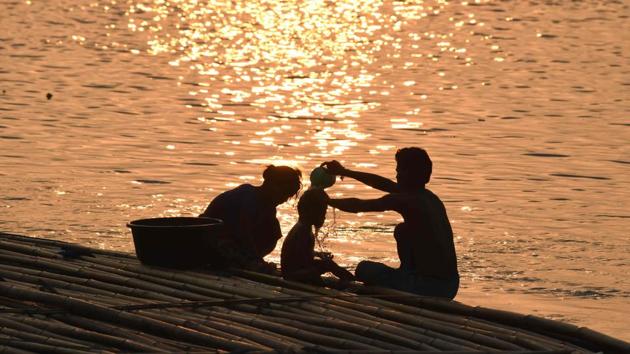 A man bathes his child at sunset while sitting on a floating bamboo for sale along the river Brahmaputra, in Guwahati, Assam. (Biju Boro / AFP)