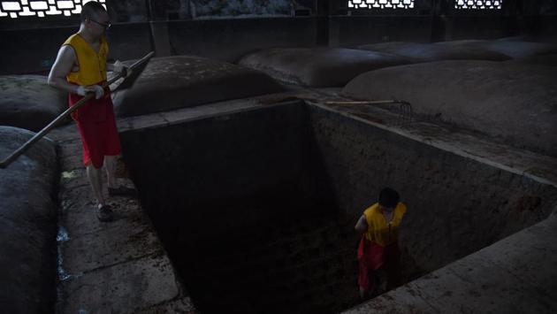 An employee works inside a depression that holds fermenting grain to produce baijiu. Emboldened distilleries are now looking abroad, staging tastings and developing smoother, export-oriented brands, while touting centuries-old artisanal production methods. At Luzhou Laojiao, sorghum is fermented for months in deep microbe-rich earthen pits, some in continuous use since 1573. (Hector Retamal / AFP) An employee works inside a depression that holds fermenting grain to produce baijiu. Emboldened distilleries are now looking abroad, staging tastings and developing smoother, export-oriented brands, while touting centuries-old artisanal production methods. At Luzhou Laojiao, sorghum is fermented for months in deep microbe-rich earthen pits, some in continuous use since 1573. (Hector Retamal / AFP)