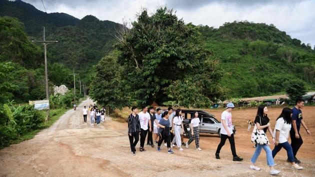 Visitors walking down the road away from the Tham Luang cave, in which 12 boys from the “Wild Boars” football team and their coach were trapped last year, in the Mae Sai district of Chiang Rai province. (Lilian Suwanrumpha / AFP)