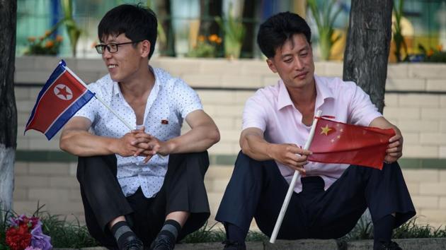 Two men sit holding North Korean and Chinese flags near Kim Il Sung square in Pyongyang, as Chinese President Xi Jinping visits the country. Xi Jinping started a historic visit in Pyongyang on June 20, to reboot a troubled alliance, as he and North Korean leader Kim Jong Un face their own challenges with US President Donald Trump. (Ed Jones / AFP)