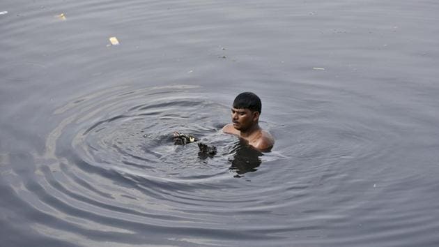 A scavenger sifts for valuables. On the neighbouring ghat, octogenarian Ram Nath has been performing aartis twice a day for over five decades. Before he prepares for the aarti, he washes his hands, feet and face with the river water. “I know the river has become extremely dirty, as several drains flow into it.” “But no matter how dirty the river might be, it is Goddess Yamuna for me,” he said. (Burhaan Kinu / HT Photo)