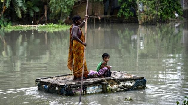 An Indian woman paddles on a tinkered boat as a child looks on at the flood-affected Kayakuchi village in Barpeta district of the Assam. (David Talukdar / AFP)