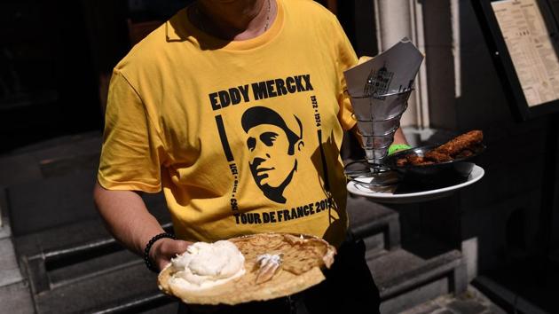 A waiter wearing a yellow T-shirt depicting Belgian legend Eddy Merckx carries food on a terrace of the Grand-Place - Grote Markt Square in Brussels. This is the 106th edition of the Tour de France with a 194.5 km stage in the region of Brussels, 100 years after the introduction of the yellow jersey and 50 years after Belgian legend Eddy Merckx won his first Tour. (Marco Bertorello / AFP) A waiter wearing a yellow T-shirt depicting Belgian legend Eddy Merckx carries food on a terrace of the Grand-Place - Grote Markt Square in Brussels. This is the 106th edition of the Tour de France with a 194.5 km stage in the region of Brussels, 100 years after the introduction of the yellow jersey and 50 years after Belgian legend Eddy Merckx won his first Tour. (Marco Bertorello / AFP)