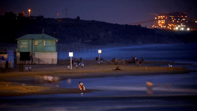 A power station is seen in the background as beachgoers are seen along the shore of the Mediterranean Sea in the evening at a beach in Ashkelon, Israel. (Amir Cohen / REUTERS)