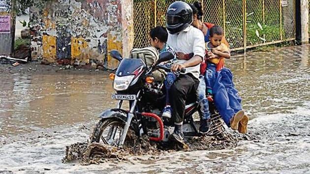 A family on a motorcycle makes its way through a waterlogged road at Sector 22/23 Chowk after light rain on Monday.(Yogendra Kumar/HT)