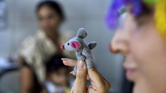 A clownselor entertains a child-patient. “We have been here for the last five months and they come every Saturday. The mood of the entire ward changes when they are here. It also distracts from the depressing environment,” said Shivam’s mother, adding that it helps her de-stress as well. (Ravi Choudhary / PTI) 