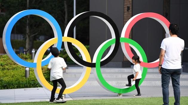 A man takes a photo of children next to the Olympic Rings displayed at the Japan Sport Olympic Square beside the new National Stadium, still under construction. (Charly Triballeau / AFP) A man takes a photo of children next to the Olympic Rings displayed at the Japan Sport Olympic Square beside the new National Stadium, still under construction. (Charly Triballeau / AFP)