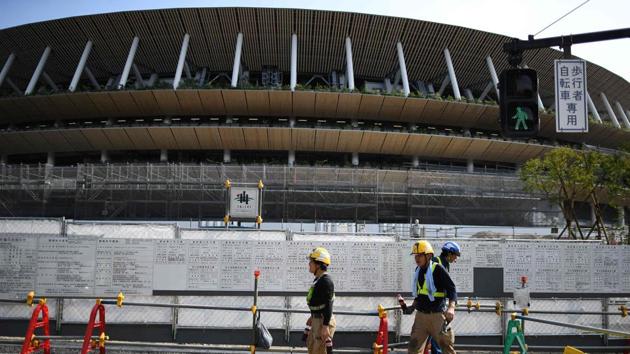 Workers walk in front of the new National Stadium.The Summer Olympics will return to Tokyo next year for the first time since 1964. (Charly Triballeau / AFP) Workers walk in front of the new National Stadium.The Summer Olympics will return to Tokyo next year for the first time since 1964. (Charly Triballeau / AFP)