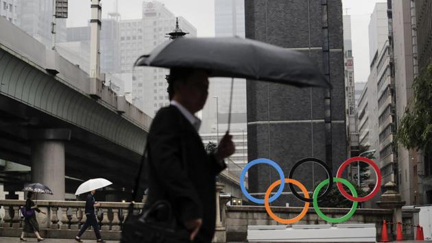 Commuters walk past the Olympic Rings in Tokyo. To mark the year-to-go stamp, the gold, silver and bronze Olympic medals were unveiled on July 23 as part of daylong ceremonies around the Japanese capital. Tokyo’s 1964 Olympics showcased bullet trains, futuristic designs and a new expressway, underlining Japan’s recovery following World War II. Those games were the first seen worldwide by early satellites, sending the Olympics into a new era. (Jae C. Hong / AP)