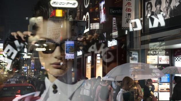 Pedestrians are seen through an advertisement as they walk along the busy streets of the Shibuya district in Tokyo. Local sponsorship revenue has passed $3 billion, about three times more than any previous games, driven by Japan’s giant advertising and marketing company Dentsu Inc., the exclusive marketing agency for the Tokyo Games caught in a French probe into alleged vote-buying connected with Tokyo winning the 2020 Olympics. (Jae C. Hong / AP)