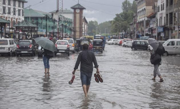 Jammu and Kashmir, July 25 (ANI): People walk in Waterlogged road after heavy rain in Srinagar on Thursday. (ANI Photo)