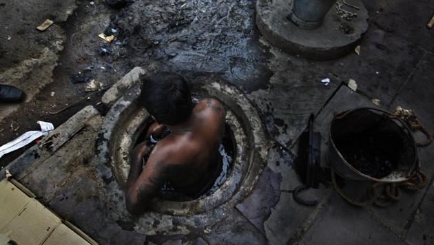 Municipal worker attempts to unblock a sewer overflowing with human excreta. (Raj K Raj / Hindustan Times)