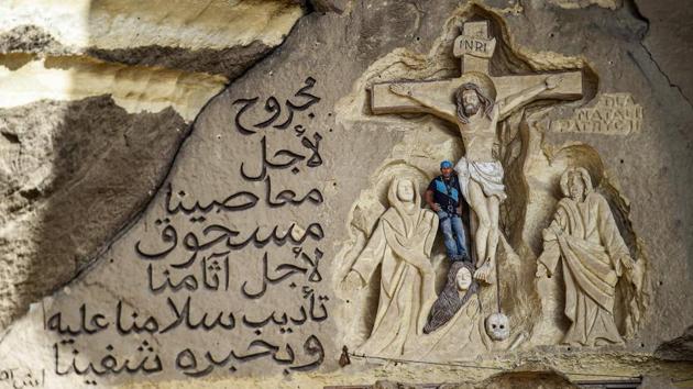 Artist Mario, sculptor of St. Simon the Tanner Monastery complex, poses for a picture alongside a scene relief depicting the Crucifixion of Jesus Christ and a verse in Arabic from the Biblical Book of Isaiah. Mario spent more than two decades carving the rugged insides of the seven cave churches and chapels of the rock-hewn St. Simon Monastery and church complex atop Cairo’s Mokkatam hills, with designs inspired by biblical stories. (Mohamed el-Shahed / AFP) Artist Mario, sculptor of St. Simon the Tanner Monastery complex, poses for a picture alongside a scene relief depicting the Crucifixion of Jesus Christ and a verse in Arabic from the Biblical Book of Isaiah. Mario spent more than two decades carving the rugged insides of the seven cave churches and chapels of the rock-hewn St. Simon Monastery and church complex atop Cairo’s Mokkatam hills, with designs inspired by biblical stories. (Mohamed el-Shahed / AFP)