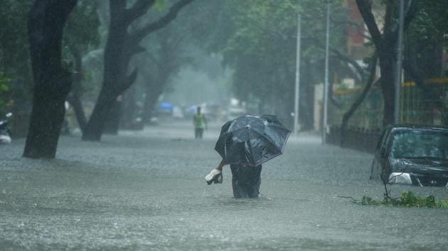 Man seen wading through an inundated road with his shoes in hand. 