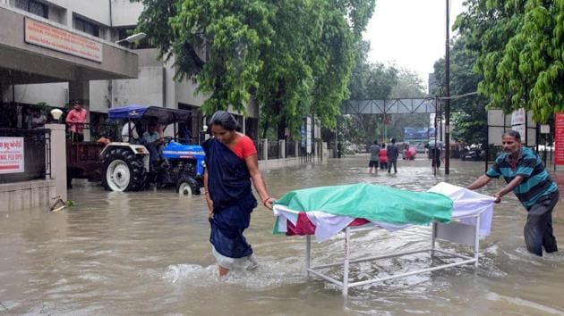 Two workers push a stretcher where lies a dead body as they wade through the waterlogged campus of a hospital in Vadodara. The Gujarat city got flooded due to very heavy rains on July 31, through water coming from Ajwa Dam and Vishwamitri river. (STR / AFP) Two workers push a stretcher where lies a dead body as they wade through the waterlogged campus of a hospital in Vadodara. The Gujarat city got flooded due to very heavy rains on July 31, through water coming from Ajwa Dam and Vishwamitri river. (STR / AFP)