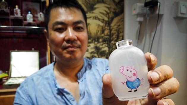 An artist Wei Dongfang showing a small bottle with the design of Pegga Pig at his workshop on Nanluoguxiang Street in the centre of Beijing.(AFP)