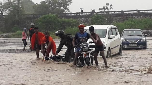 Commuters trying to hold the bikes in the flooded water stream near Rajaji National Park, Uttarakhand. (ANI File) Commuters trying to hold the bikes in the flooded water stream near Rajaji National Park, Uttarakhand. (ANI File)