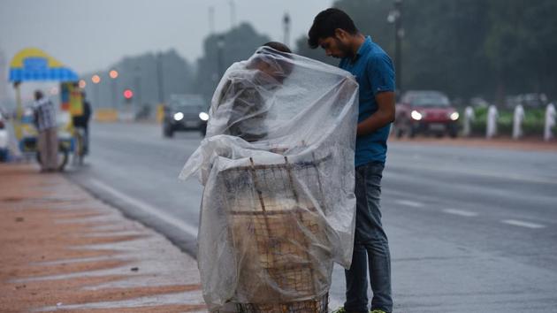 A vendor covered in plastic tarp sells snacks during a rain shower at Rajpath in New Delhi. The Safdarjung Observatory in South-Central Delhi had recorded 12.6 mm rainfall till 8:30 am. Palam observatory in the South-West Delhi received the highest, 38.5 mm rain till 8.30 am. Other weather stations recorded --- Delhi Ridge (21.6 mm), Ayanagar (17.6 mm) and Lodhi Road (15.4 mm) rainfall. (Vipin Kumar / HT Photo) 