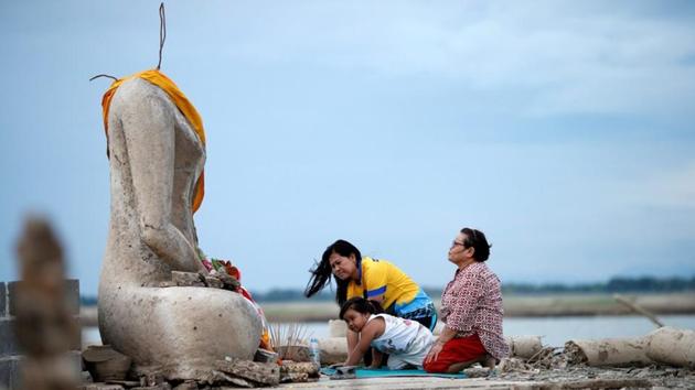 A family prays near the ruins of a headless Buddha statue, which has resurfaced in a dried-up dam due to drought, in Lopburi, Thailand.(REUTERS) A family prays near the ruins of a headless Buddha statue, which has resurfaced in a dried-up dam due to drought, in Lopburi, Thailand.(REUTERS)