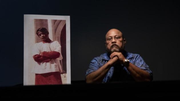 Melvin Duenas, 58, sits beside a photo of himself when he was 11 years old, the age when he says in a lawsuit he was sexual abused by Tomas Camacho and Louis Brouillard, both Catholic priests at the churches where Duenas served as an altar boy. “We were taught that when we see a priest we run over there and kneel down,” said Duenas. “We looked at them as God himself.” (David Goldman / AP) Melvin Duenas, 58, sits beside a photo of himself when he was 11 years old, the age when he says in a lawsuit he was sexual abused by Tomas Camacho and Louis Brouillard, both Catholic priests at the churches where Duenas served as an altar boy. “We were taught that when we see a priest we run over there and kneel down,” said Duenas. “We looked at them as God himself.” (David Goldman / AP)