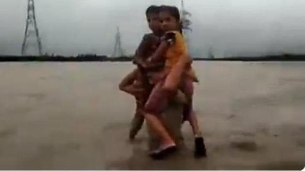 A video of Gujarat police constable Pruthviraj Jadeja walking through waist-deep water with the two kids on his shoulders has been widely shared on Twitter.(Vijay Rupani/ Twitter screengrab)