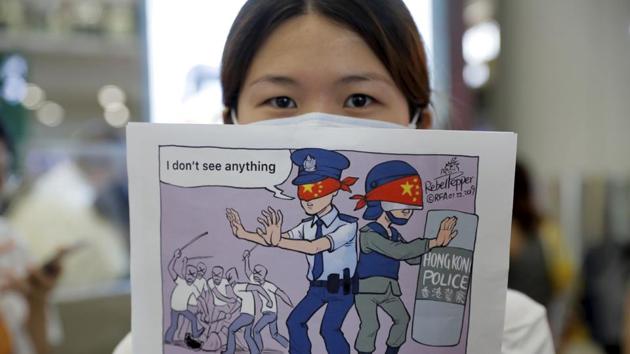 A woman holds up a cartoon depicting police feigning ignorance of thugs attacking protesters as she joins protesters during a second day of sit-in protest at the airport in Hong Kong.(AP)