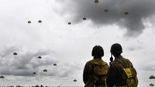 Men dressed as US GIs stand in a field as paratroopers from Britain's 16 Air Assault Brigade and France's 11th Parachute Brigade perform a jump over Sannerville, north-western France, on June 5, 2019. (AFP) Men dressed as US GIs stand in a field as paratroopers from Britain's 16 Air Assault Brigade and France's 11th Parachute Brigade perform a jump over Sannerville, north-western France, on June 5, 2019. (AFP)