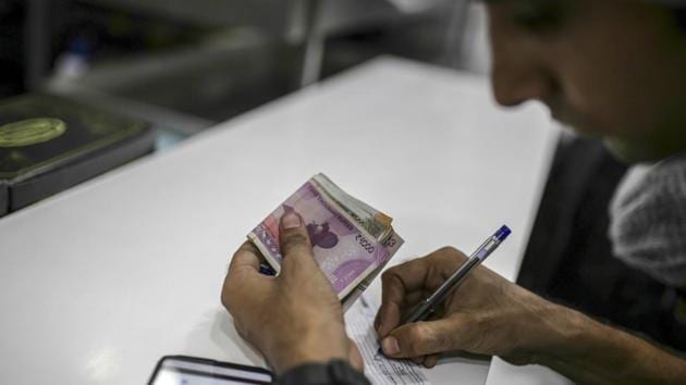 An employee holds Indian rupee banknotes while writing on a notepad. (Bloomberg) An employee holds Indian rupee banknotes while writing on a notepad. (Bloomberg)