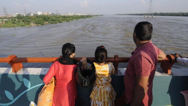 Locals watch the risen water level of Yamuna from the Yamuna bridge, in Noida. Revenue minister Kailash Gahlot tweeted that he inspected relief camps at Haathi Ghat and Kanchan Colony and interacted with people who have been evacuated and are now staying in relief camps. (Sunil Ghosh / HT Photo)
