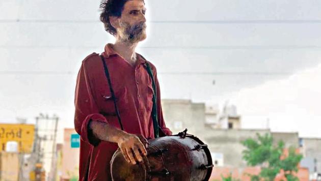 Jagdish spends his working day walking along the lanes of Gurugram bazaars, singing devotional and folk songs, playing the dholak.(HT Photo)