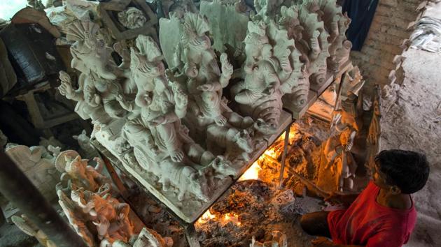 A worker tends to the fire under a batch of wet clay idols to speed up the drying process during damp monsoon days at a workshop. (Satish Bate / HT Photo) A worker tends to the fire under a batch of wet clay idols to speed up the drying process during damp monsoon days at a workshop. (Satish Bate / HT Photo)