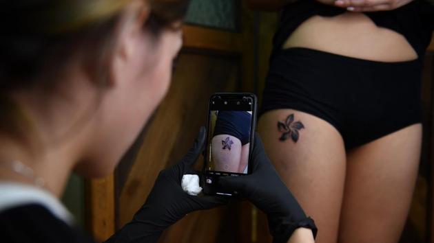 Tattoo artist Iris Lam takes a photo of her client’s fresh Bauhinia flower. The Bauhinia flower is the emblem of Hong Kong and normally coloured red, but is represented in black in C’s tattoo as a mark of the troubles clouding the city. (Lillian Suwanrumpha / AFP) Tattoo artist Iris Lam takes a photo of her client’s fresh Bauhinia flower. The Bauhinia flower is the emblem of Hong Kong and normally coloured red, but is represented in black in C’s tattoo as a mark of the troubles clouding the city. (Lillian Suwanrumpha / AFP)