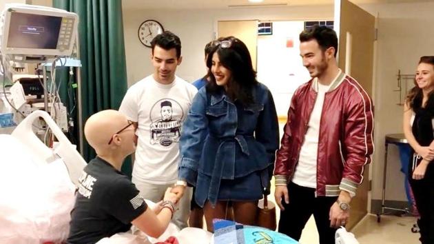 Joe, Nick and Kevin Jonas look on as cancer patient Lily Jordan interacts with Priyanka Chopra.