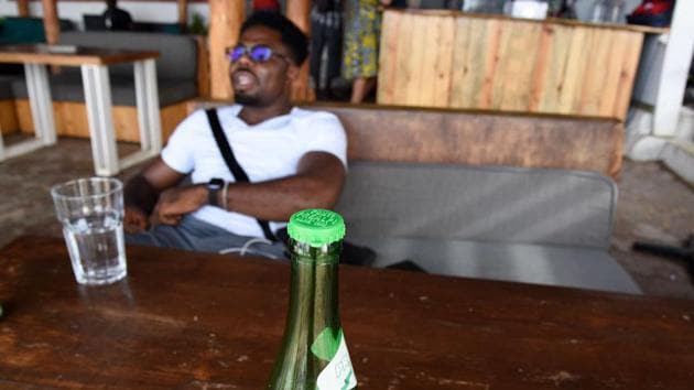 A man sits on a couch by a bottle with a collected capsule laying on a table at the Copacabana restaurant. “Every action counts,” Thiaw said. “When you know that a plastic bottle takes up to 1,000 years to decompose, how can you not use glass bottles? (Seyllou / AFP)