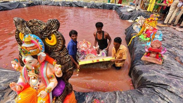 Municipal workers in Delhi help residents immerse idols in an artificial water body. In a bid to reduce the pollution load on the Yamuna river, the Delhi Pollution Control Committee (DPCC) had asked puja organisers to immerse the idols in 129 artificial ponds built at designated sites across the city. (Raj K Raj / HT Photo) 
