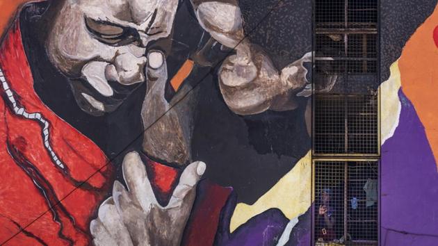 A resident looks out from the stairwell of her housing block, on which is painted an informational mural against sexual abuse, in the low income neighborhood of Mbare, known to have many supporters of former president Robert Mugabe’s ZANU-PF party.  (Ben Curtis / AP) 