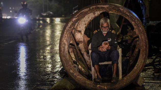 A security guard browses his mobile phone as he takes shelter inside a concrete drainage pipe during rain at Wadala in Mumbai, Maharashtra. (Kunal Patil / HT Photo)